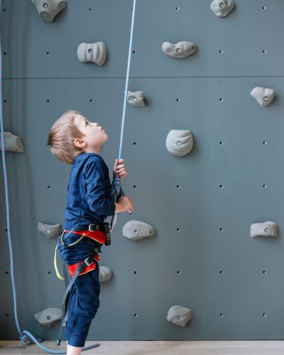 a-brave-little-climber-boy-prepares-to-climb-a-cli-2022-03-02-22-18-10-utc