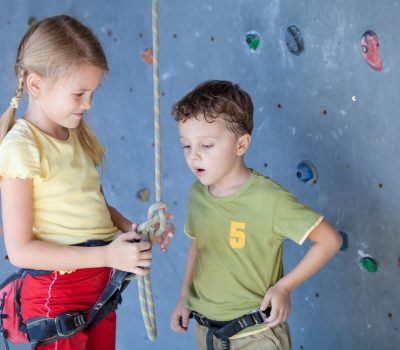 brother and sister standing near a rock wall for climbing indoor